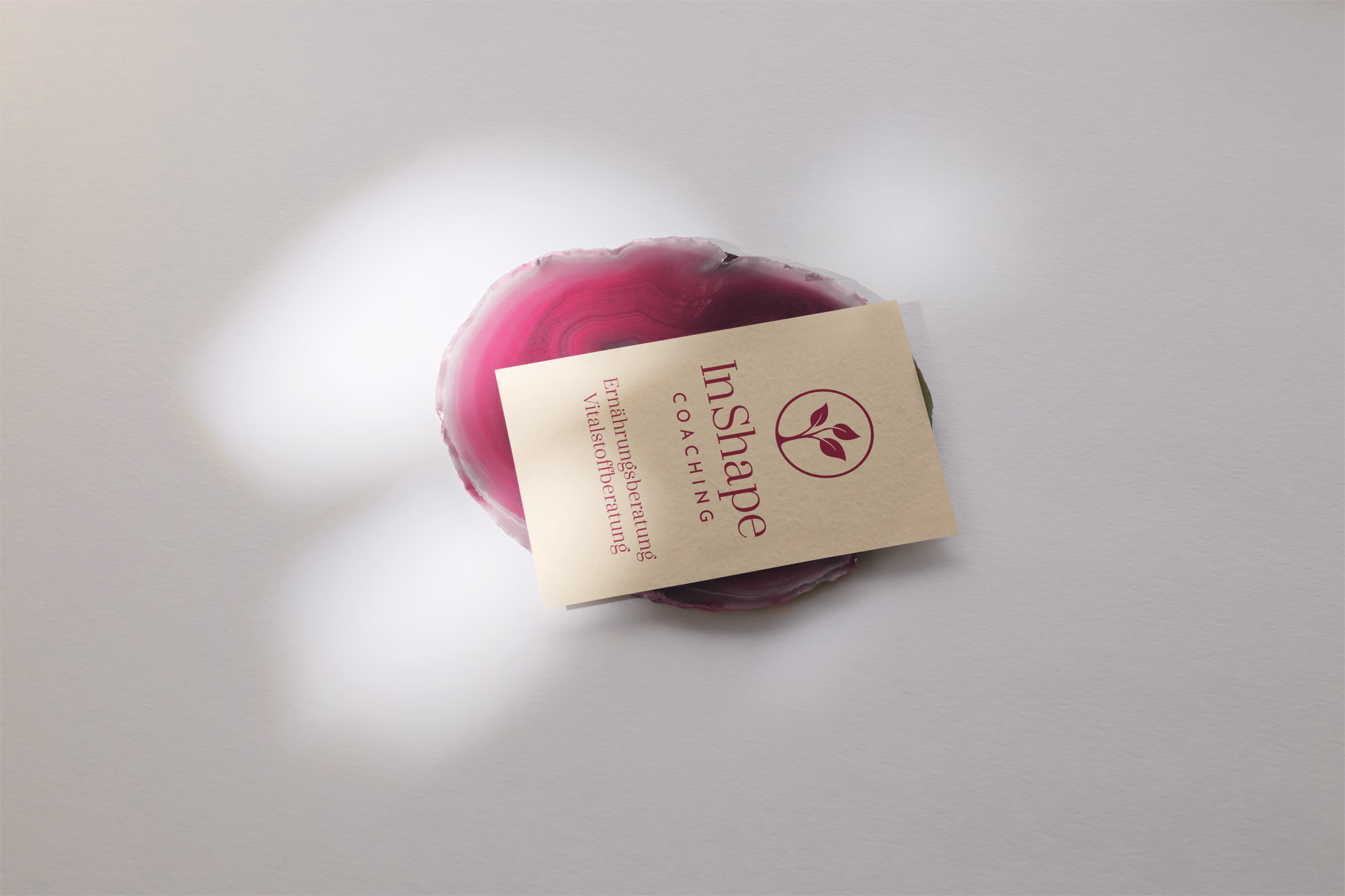 Ein rosa Agatenscheibe mit Produktetikett "InShape Coaching" auf grauem Hintergrund.