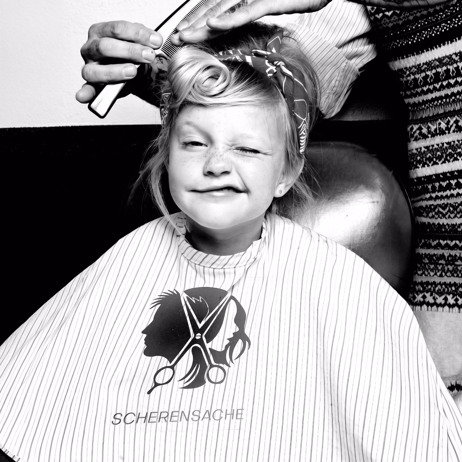 Kleines Mädchen beim Friseur, das Haar wird gekämmt, trägt Scherensache-Cape.
