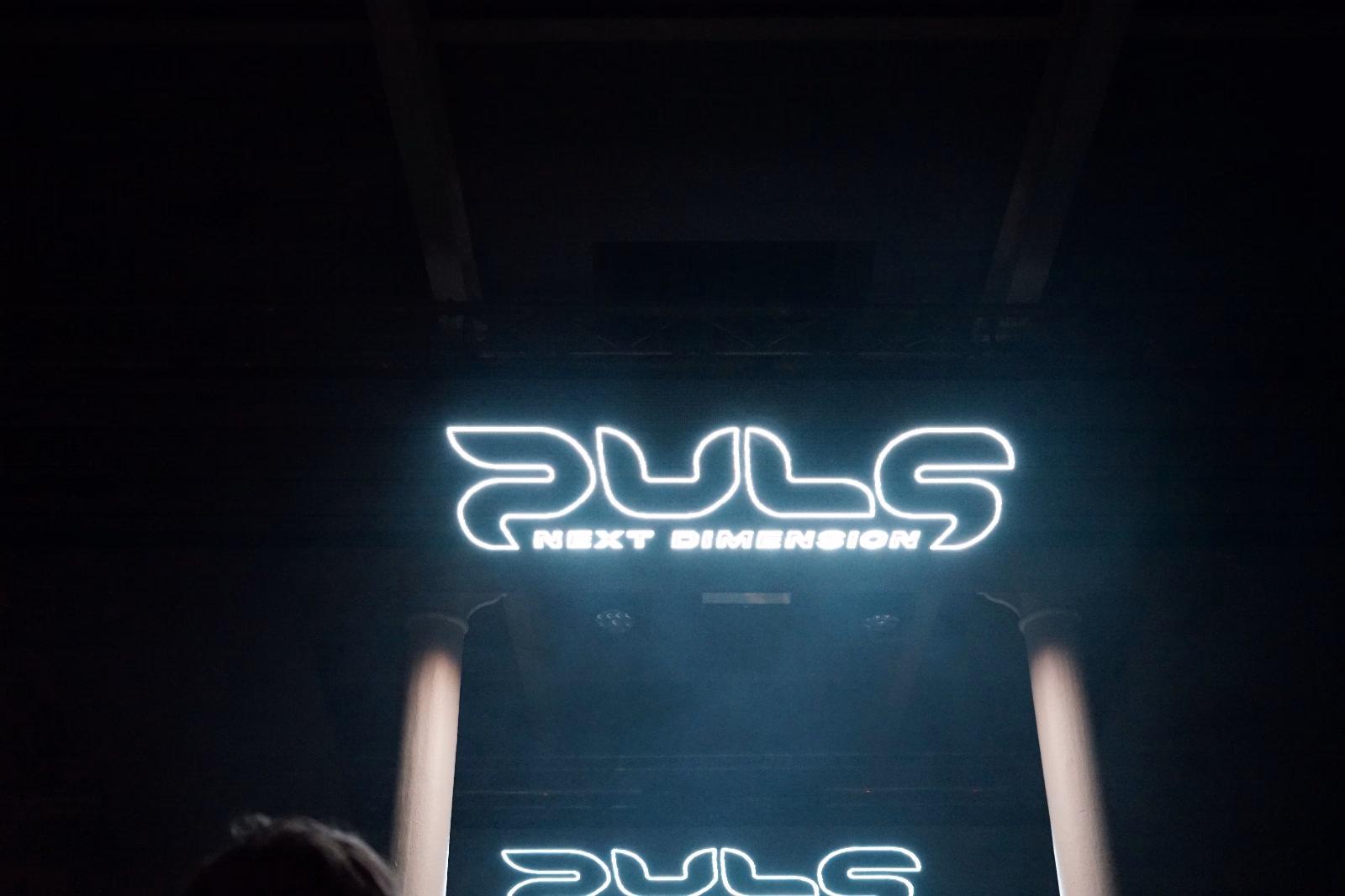 Neon-Leuchtreklame mit "PULS NEXT DIMENSION" Text auf dunklem Hintergrund in Cyan-Blau